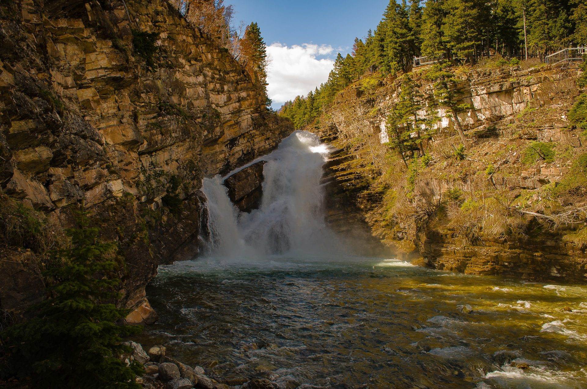 A scenic view of Cameron waterfall with brown rocks around. Cameron Falls is an iconic attraction of the Waterton National Park. It is known for its colours.