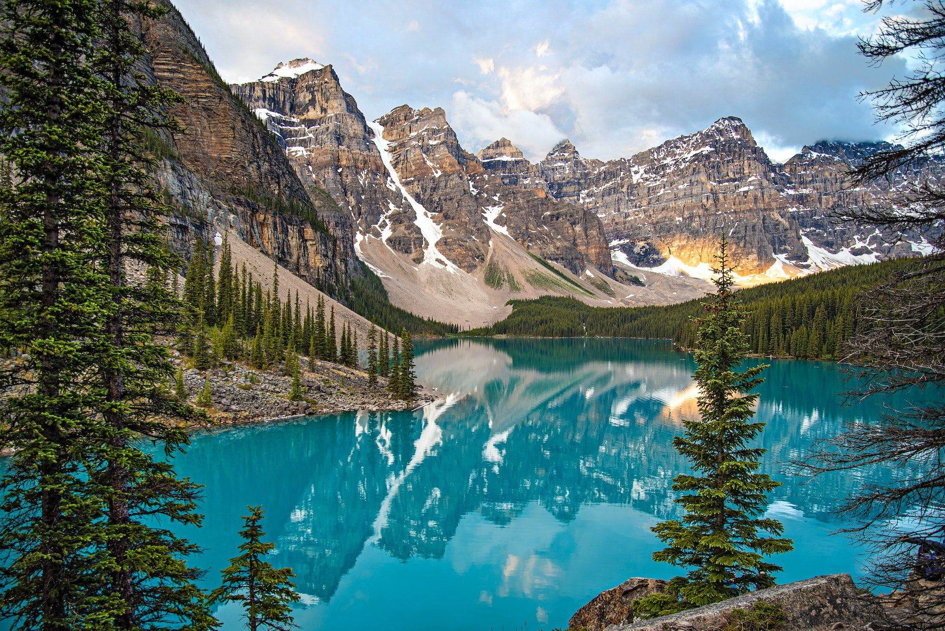 A beautiful view of Waterton Lake with a bright blue-coloured water stream and brown mountains and tall green trees around, located inside Waterton National Park.