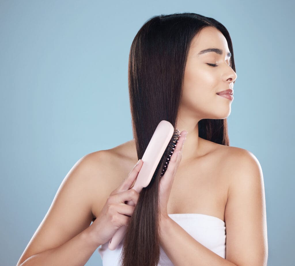 A picture of a woman in a towel combing her hair with a hairbrush on a plain blue background.