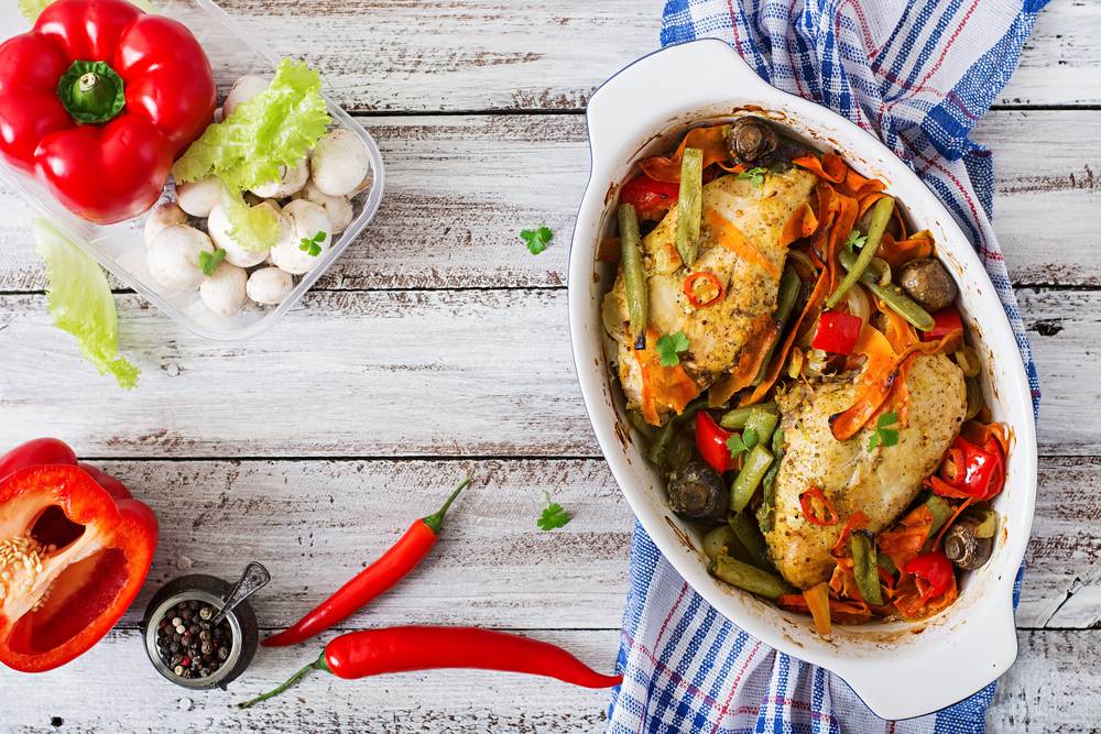 An aerial view of healthy chicken cuisine is kept on a wooden table with vegetables kept alongside.