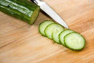 A cucumber half sliced on a chopping board and knife kept by the side. Consume raw to acquire the health benefits of cucumber.