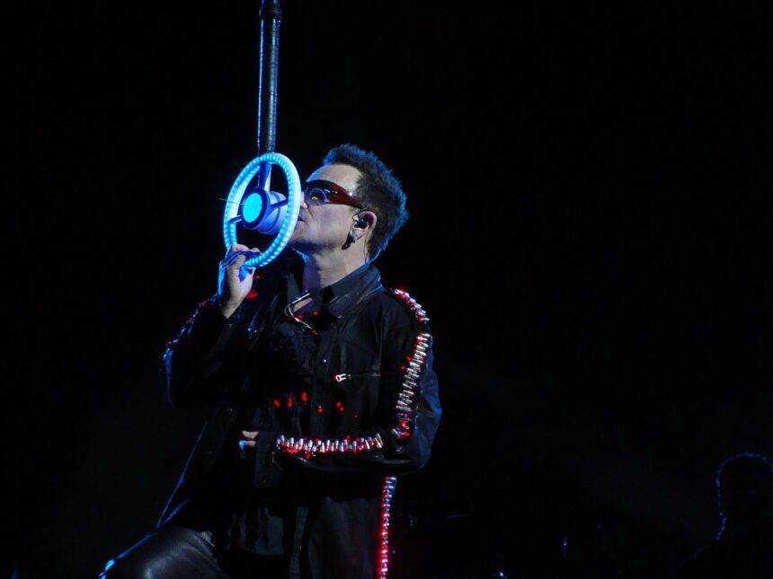 A person wearing sunglasses and singing on a neon mic in dark background.