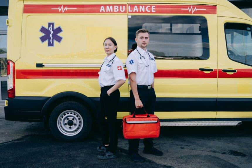 Two medical officials standing next to each other while an ambulance standing behind them.