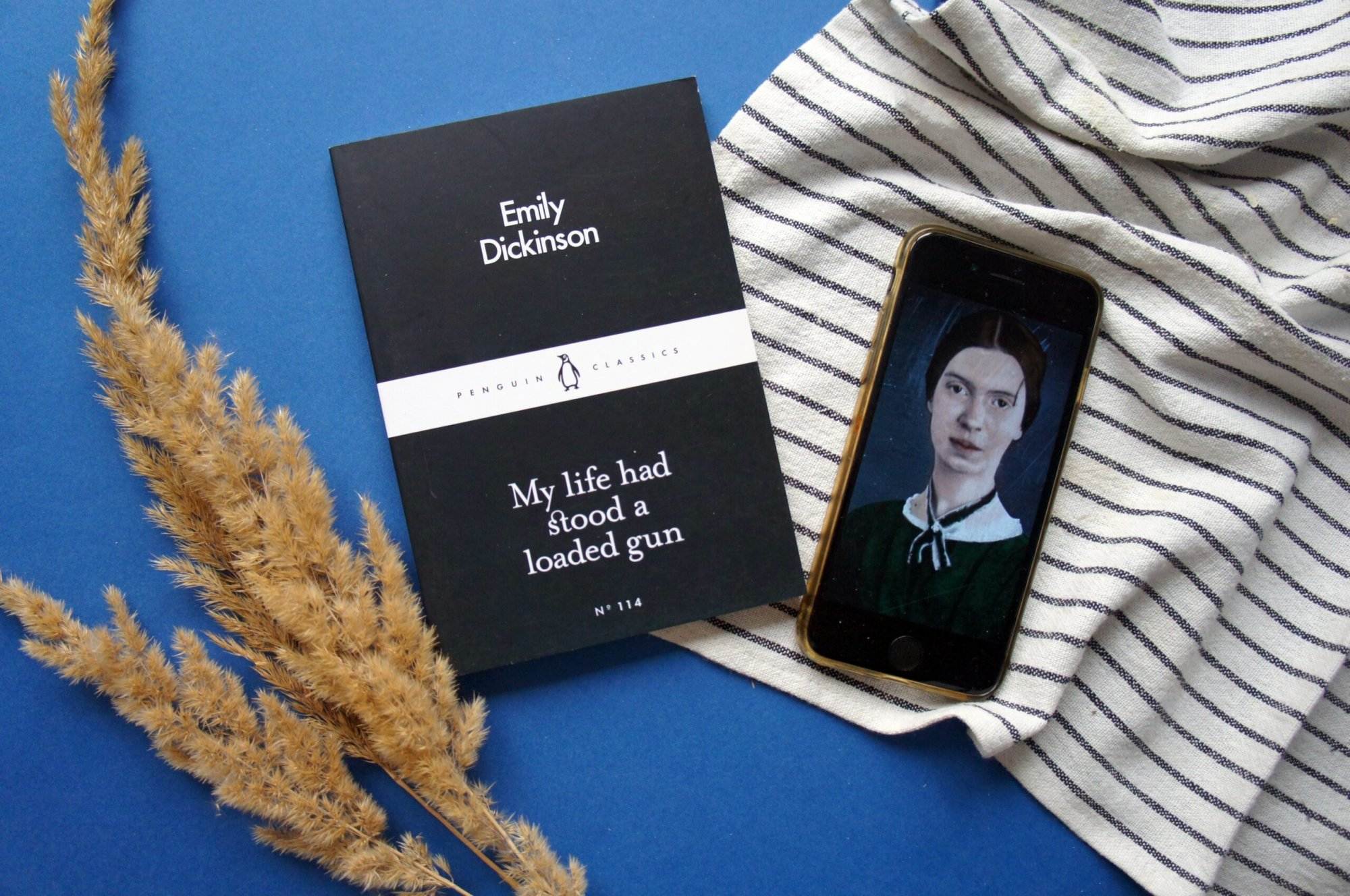 "My Life had stood a loaded gun" book by Emily Dickinson and a picture of Emily Dickinson on an android phone on a blue background.