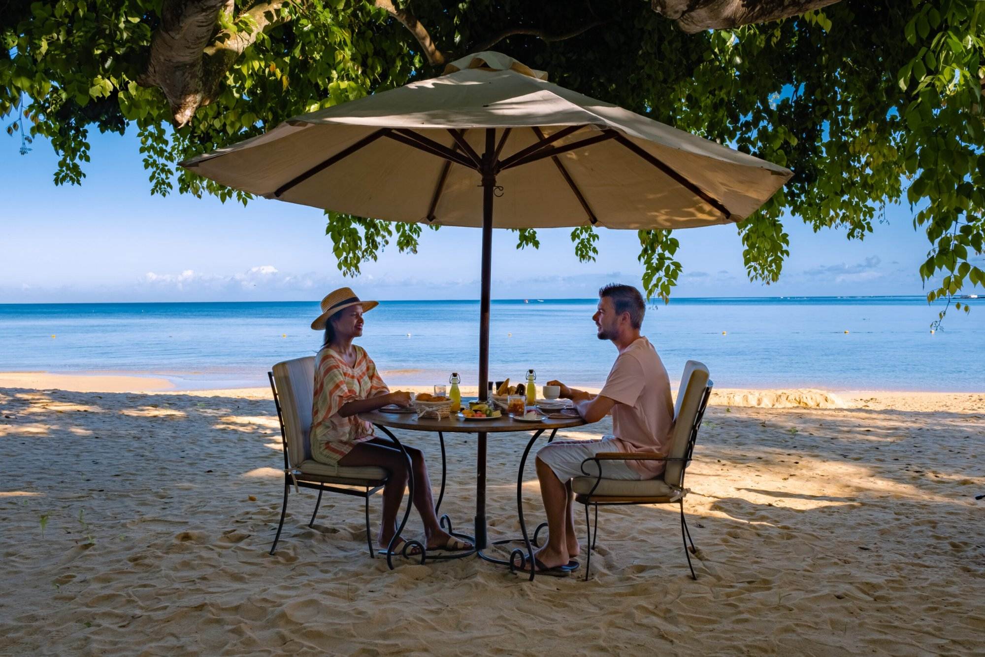 A couple sitting at a table on the seashore of a beach resort.