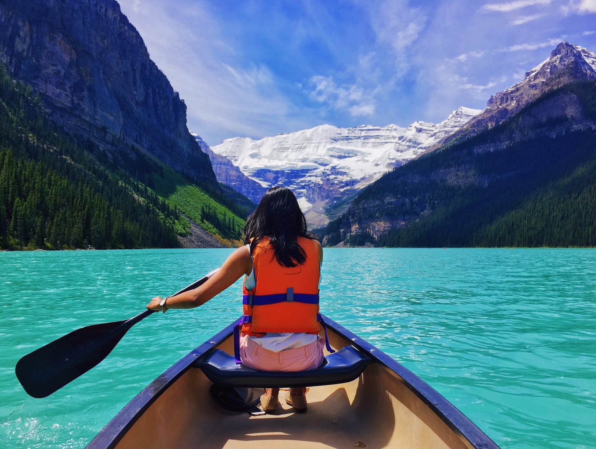 A woman rowing and riding a boat near Alberta mountains at Lake Louise.
