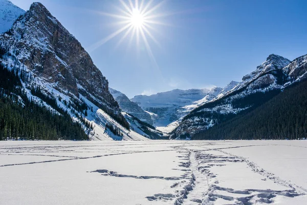 A view of frozen Louise Lake with black and white mountains at the back.