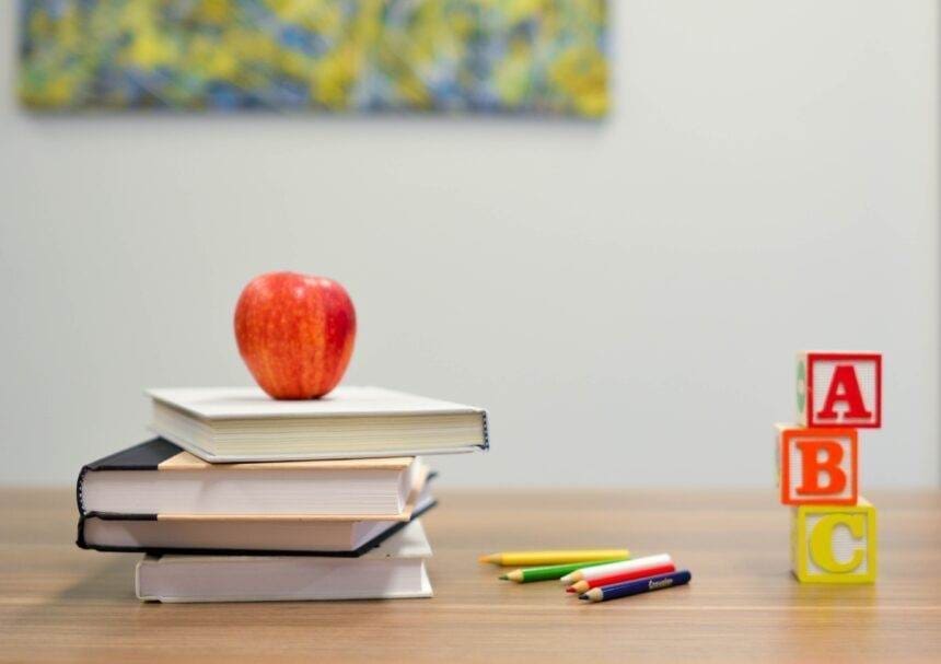 An apple is kept on a stack of books on a table and other stationery is kept alongside.