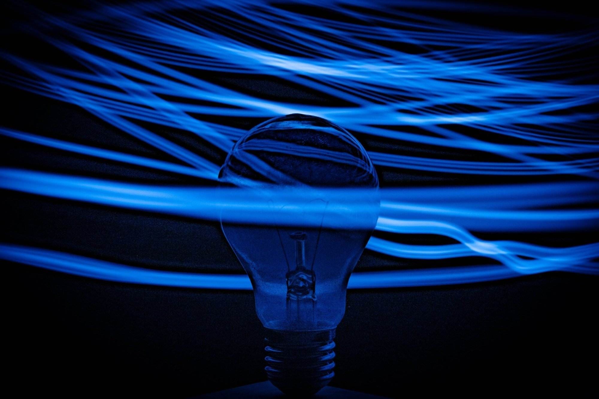 An unlit bulb with a blue ray of colors moving around it in black background.