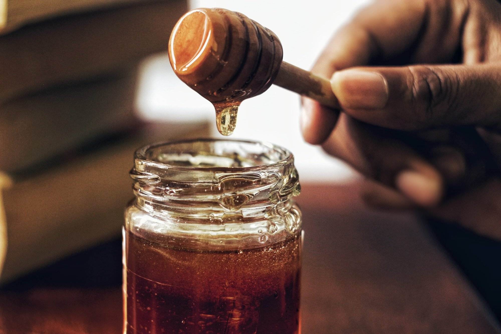 a close-up of a honey jar with the dipper pouring the honey.
