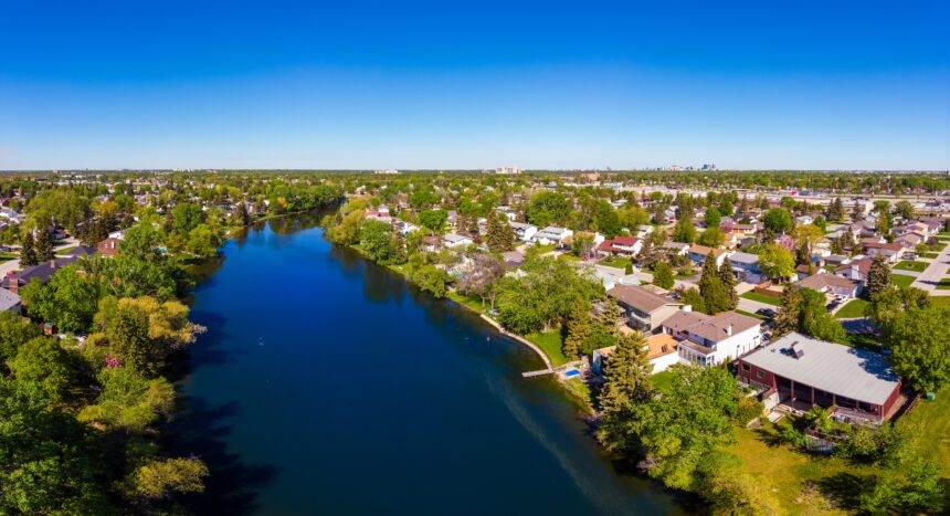 A drone view of a river and green land of grasses and trees in Winnipeg.
