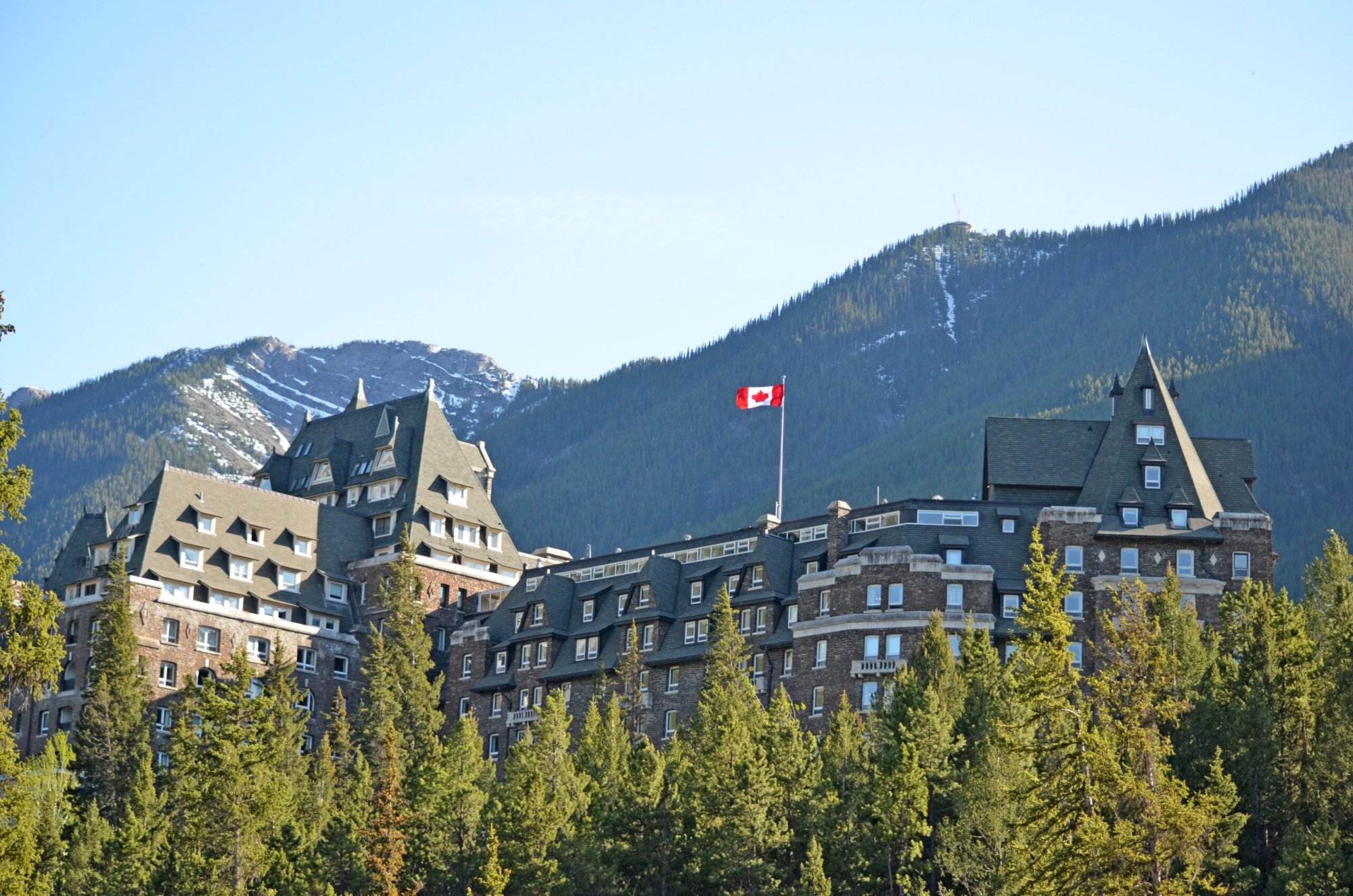 A scenic view of Fairmont Banff Springs Hotel and the Canadian flag on top.