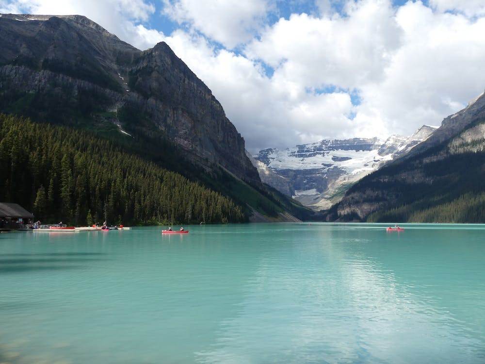 Few people in their kayaks in the Lake Louise with mountains in the background.