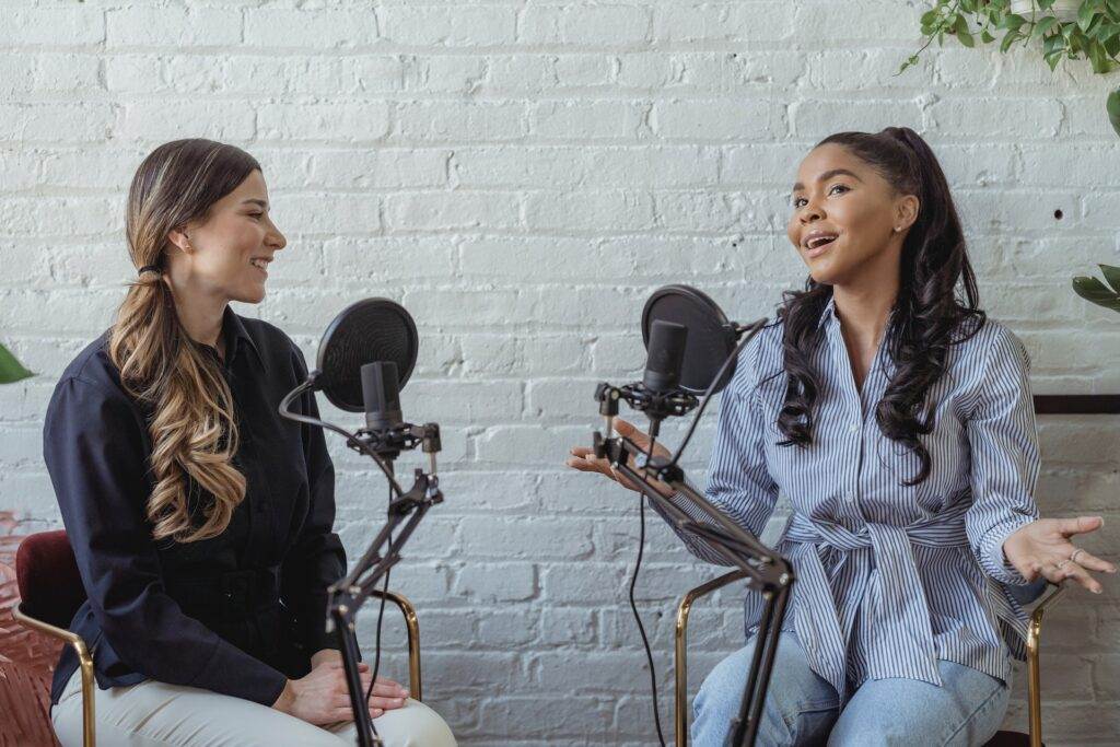 Two women recording on mics for radio advertising.
