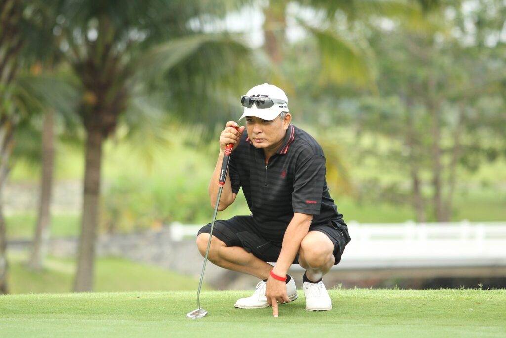 A person sitting on the ground of the golf field looking for measurements.