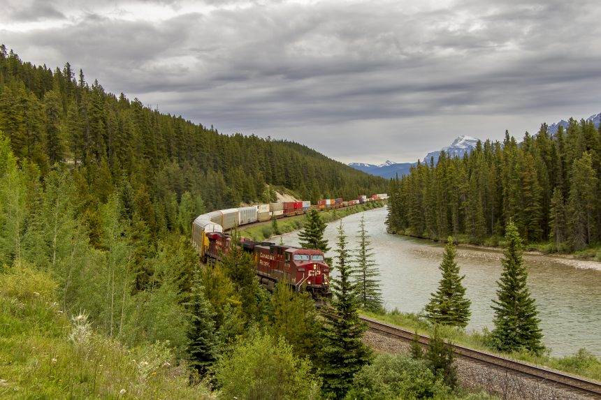 A train coming on the railway line in the Banff National Park with mountains in the background.