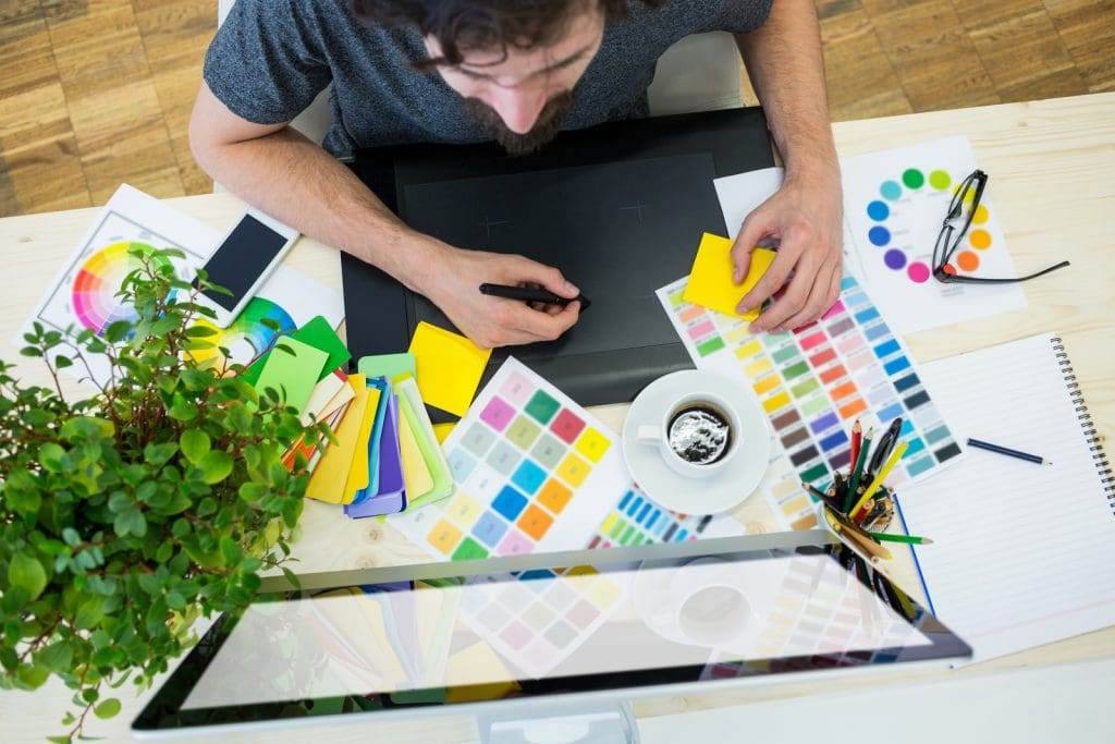 A top view of a person working with some colour palette and a laptop.