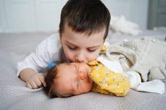An older brother kissing the head of the infant brother.