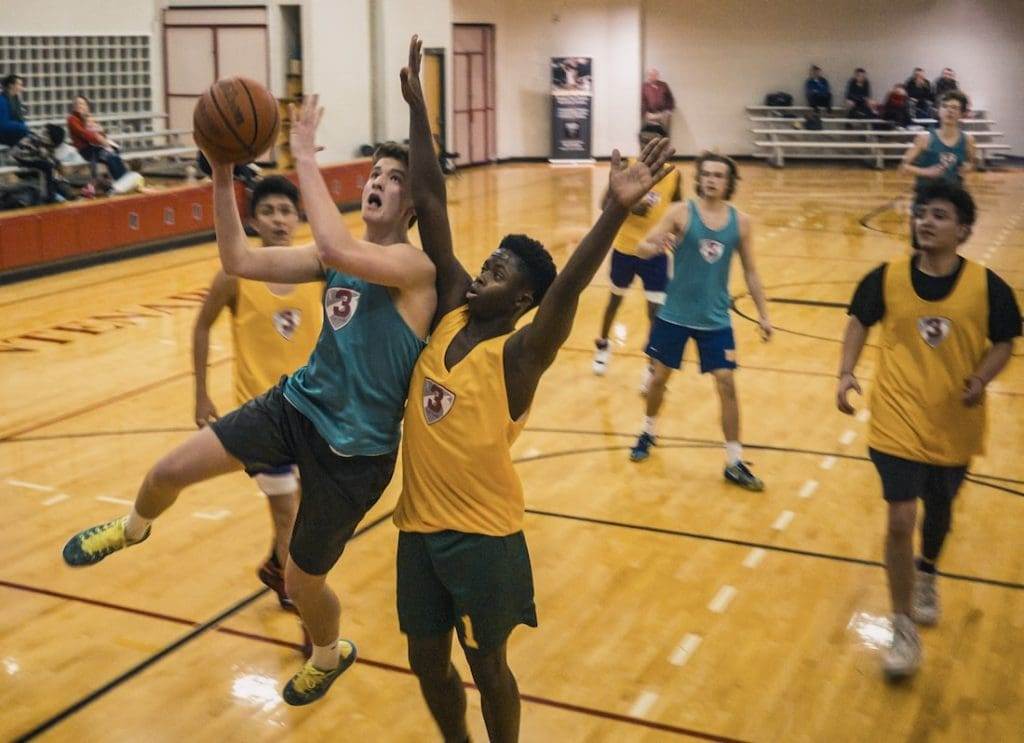 Two teams of people playing basketball in an indoor basketball court.