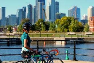 A woman with her bike standing on the side of a waterbody.