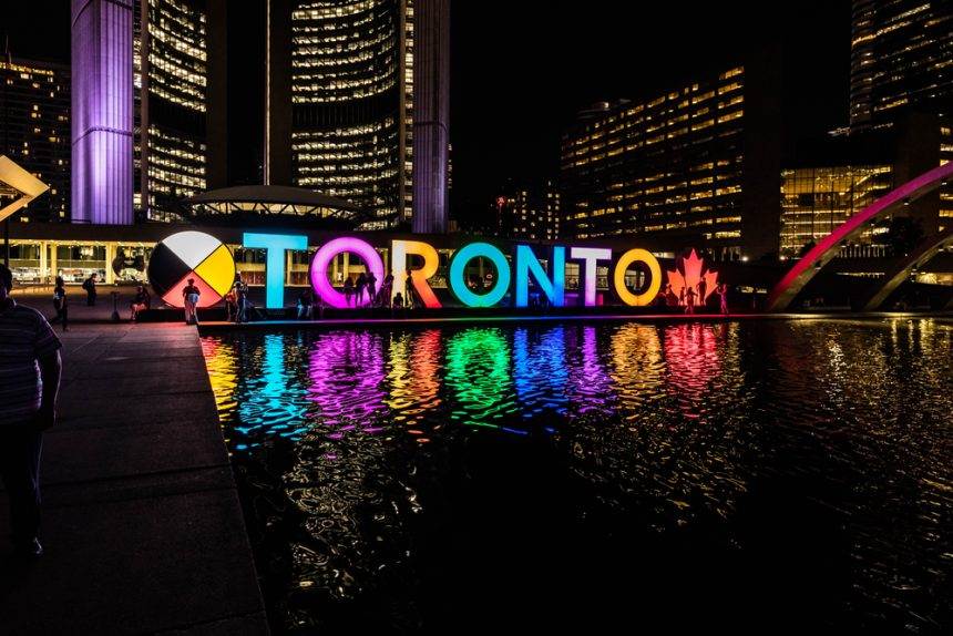 Toronto cityscape at night with illuminated sign and reflections.