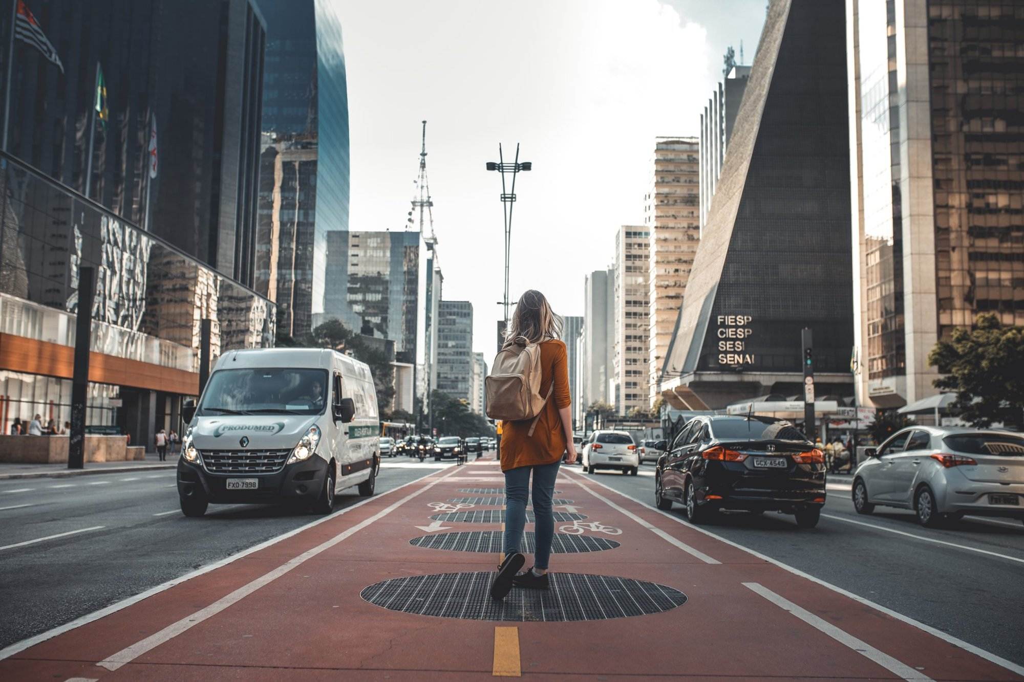 photography of woman walking along the road between vehicles