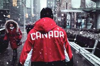 Image showing a guy walking, wearing a jacket labelled Canada on it.