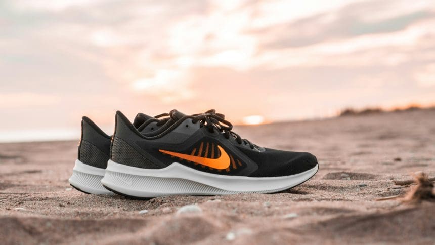 Black and orange Nike sneakers on sandy beach at sunset.